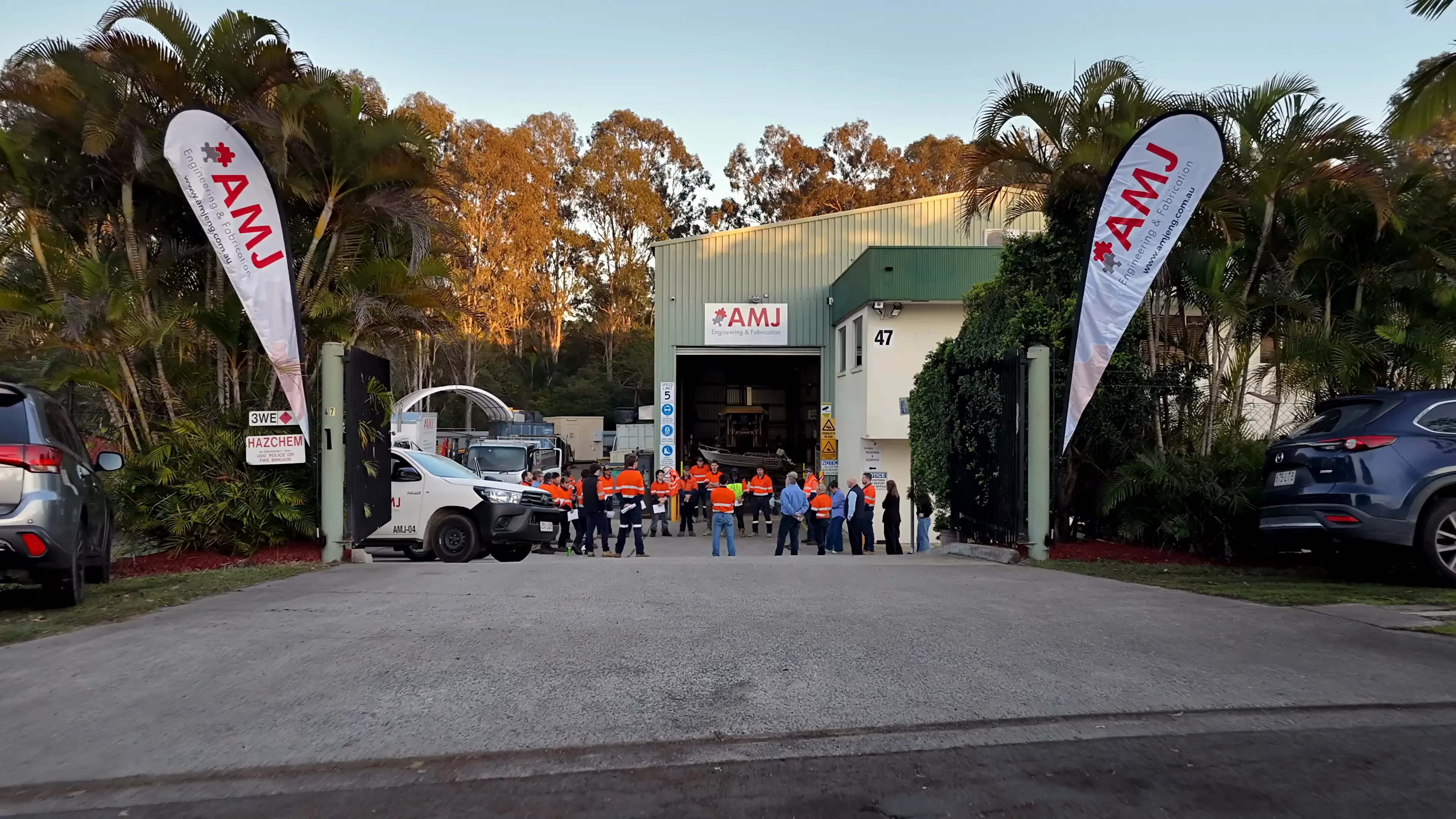 The AMJ team at the entrance of 47 Proprietary St, Tingalpa, between two AMJ teardrop banners